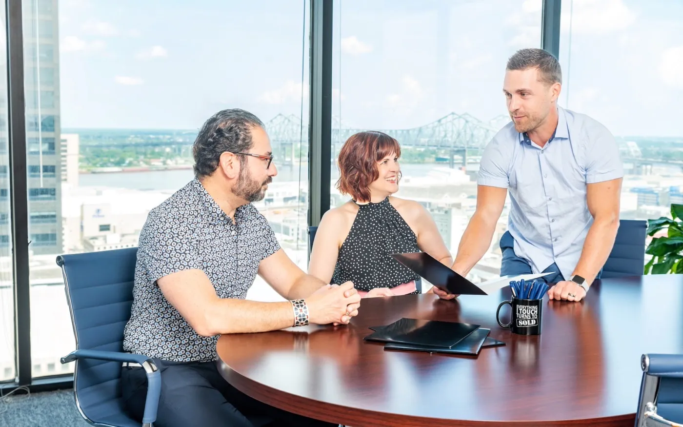 Alex Shafirovich reviewing documents with clients at a conference table, the river bridge visible through the windows behind them